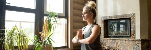 woman eyes closed meditate beside plant pots heaters in quiet peaceful living room