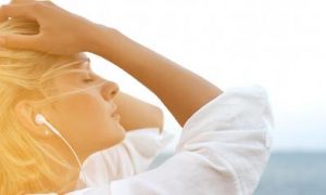 woman wearing earphones hands on hair eyes closed thinking in sunny sky