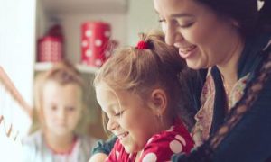 woman happily plays with daughter while another little girl sitting looking at home