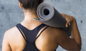 woman stands facing backward carrying yoga mat