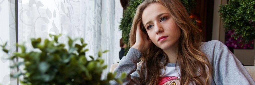 young woman sitting beside window plant pot thinking worrying