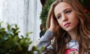 young woman sitting beside window plant pot thinking worrying