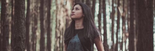 woman walks alone in forest looking at sky