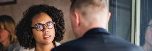 curly black hair woman sits in coffee shop talking to college