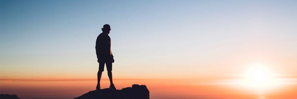 man stands on rock watching beautiful sunset