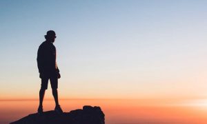 man stands on rock watching beautiful sunset