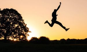 person shadow excitedly raises hand jumping over grass in sunny sky