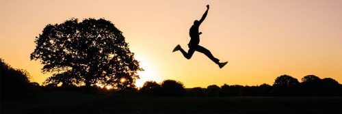 person shadow excitedly raises hand jumping over grass in sunny sky