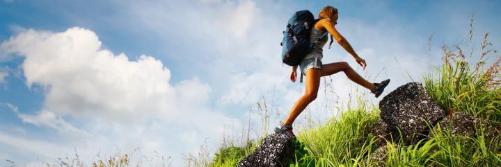 man wearing large blue back bag walks on rock in blue cloudy sky