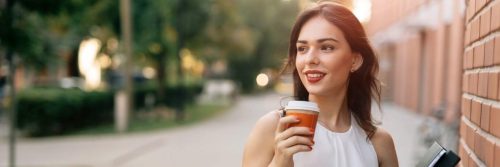 woman stands on street holding coffee cup smiling