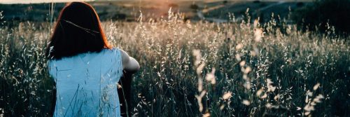 woman sits on field facing backward looking at sunny sky