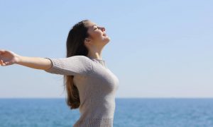 woman stands beside blue ocean closed eyes gratitude life in blue clear sky