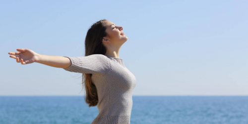 woman stands beside blue ocean closed eyes gratitude life in blue clear sky