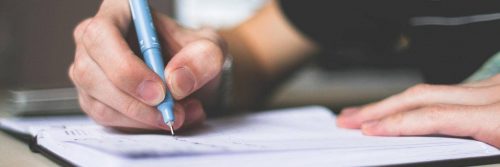 hand holding blue pen writing on notebook