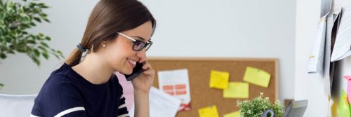 woman happily smiles answering phone while sitting in office