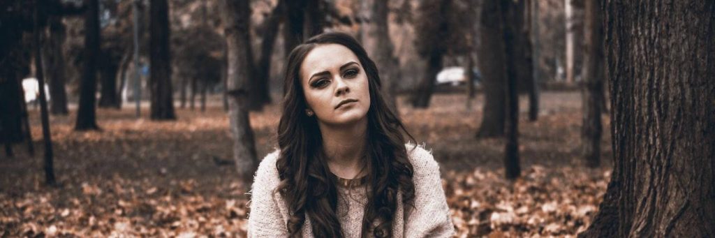 woman stands alone in forest with sad unhappy face thinking