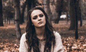 woman stands alone in forest with sad unhappy face thinking