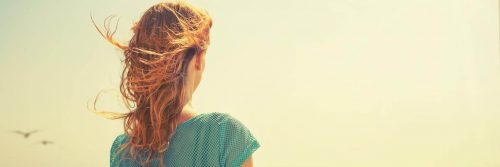 woman stands facing backward watching sunny sky