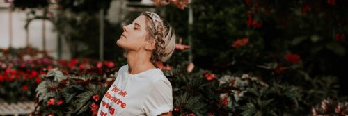 woman stands beside red flower garden closing eyes breathing