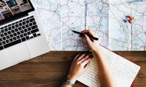 woman hands holding black pen pointing at map next to laptop glass of water