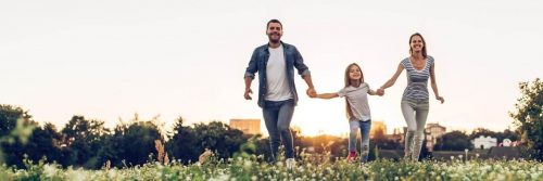 parents hold daughter hands happily walking on field smiling in sunny sky