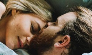 couple hugs lies on bed while man kissing on partner forehead