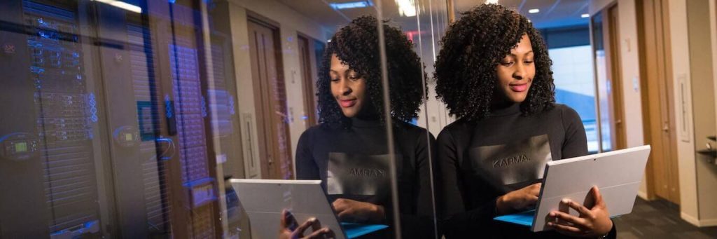 curly hair woman carrying laptop stands next to wall in office