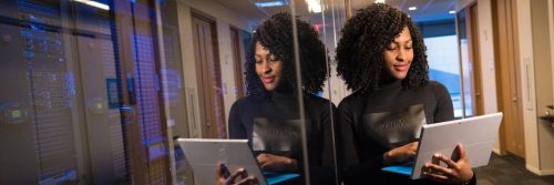 curly hair woman carrying laptop stands next to wall in office