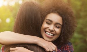 curly hair woman hugging college smiling happily in sunny sky