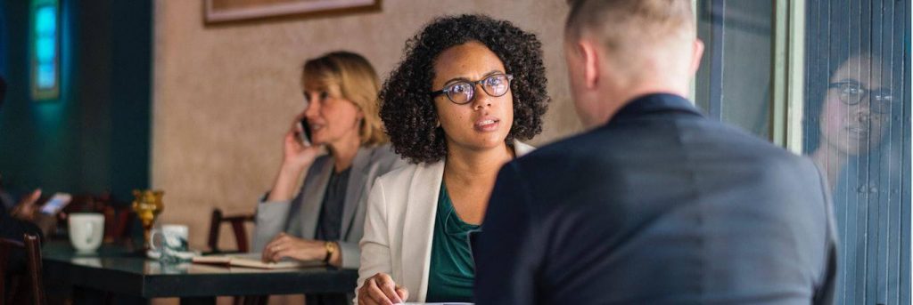 curly black hair woman sits in coffee shop seriously talking to college