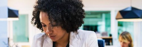 curly black hair woman wearing white vest sits in office focusing on work