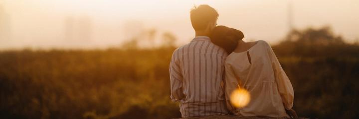 couple facing backward sits on field while woman lying on boyfriend shoulder