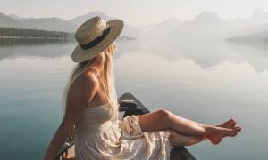 woman sits on boat in peaceful lake looking at mountain foggy sky