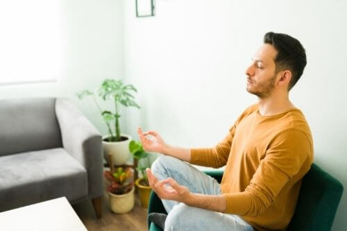 Man in mustard top sitting meditating in the office in a peaceful way.