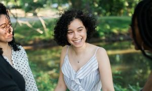 four young women standing in park beside lake speaking laughing