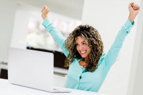 Excited woman in teal top sitting at a computer happy about abundance.