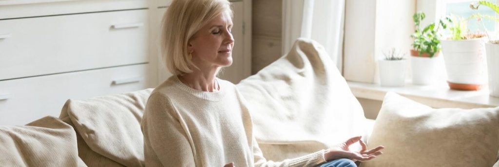 elderly woman sits on couch focuses on meditation breathing in living room