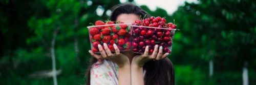 woman lifts strawberry cheery boxes stands in forest