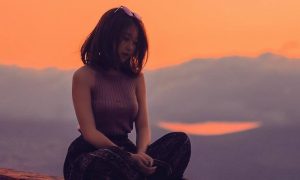 woman sits legs crossed on rock thinking in sunset cloudy sky