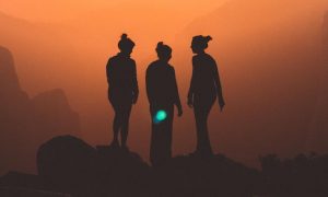 three women stand on rock in dark red sky