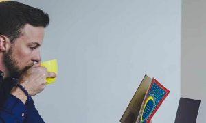 man sits in office drinking in yellow mug while reading book