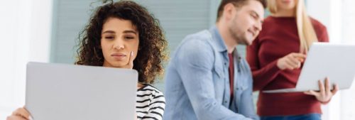 girl looking at laptop thinking while two colleges discussing pointing at laptop