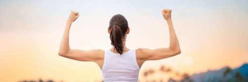 woman stands facing backward showing off muscles in sunset sky