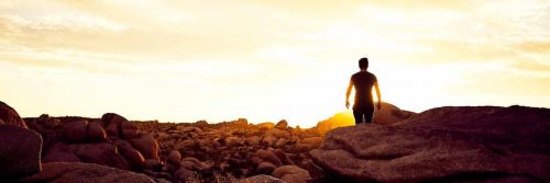 man walking between rocks in sunny sky