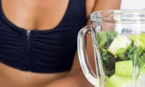 woman wearing sports bra make detox juice in blender