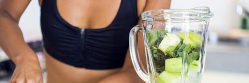 woman wearing sports bra make detox juice in blender