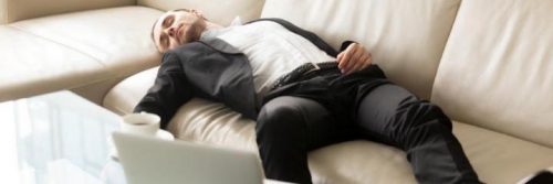 man tiredly sleeps on couch beside laptop coffee mug