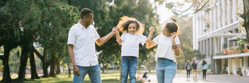 parents hold little daughter hands walking in park