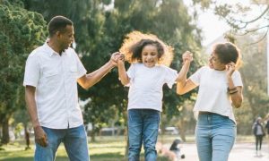 parents hold little daughter hands walking in park