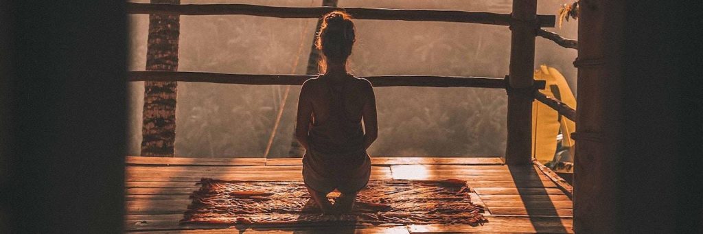 woman facing backward sits focusing on meditation on balcony